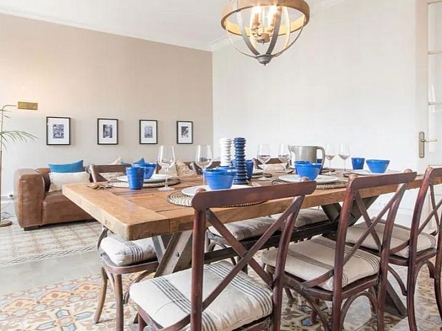 Comedor con mesa de madera, sillas blancas y lámpara de araña