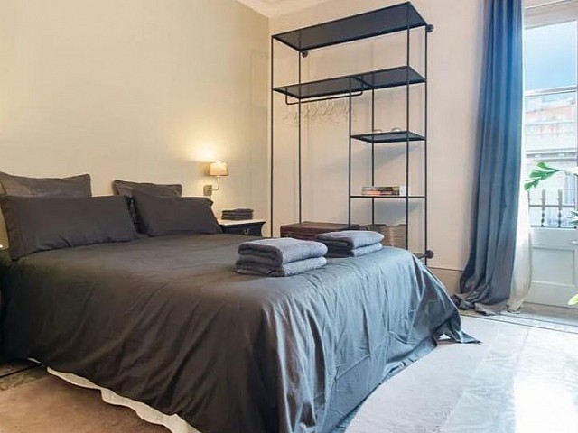 Dormitorio con cabecero oscuro, estantería y salida a terraza