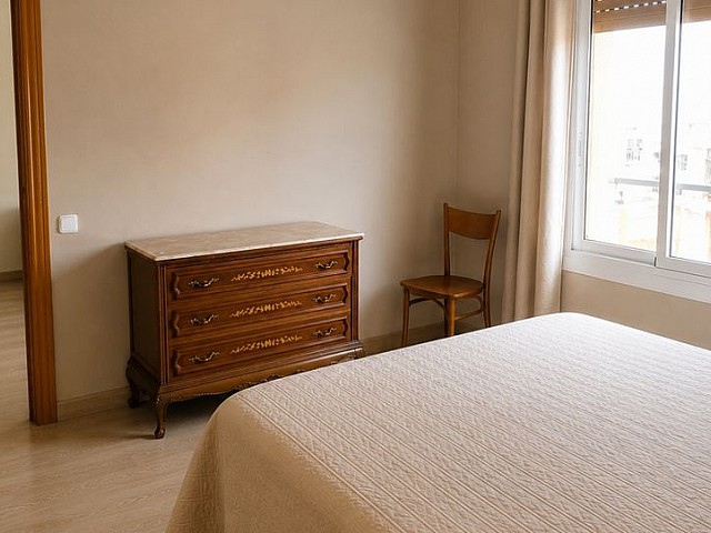 Dormitorio con cómoda de madera, cama y ventana con vistas a los tejados