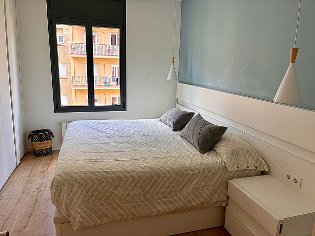 Perspectiva del dormitorio principal mostrando la cama doble, el ventanal exterior y la iluminación ambiental.