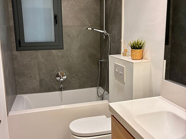 Zona de ducha moderna con alicatado gris oscuro, grifería cromada y ventana oscilobatiente.