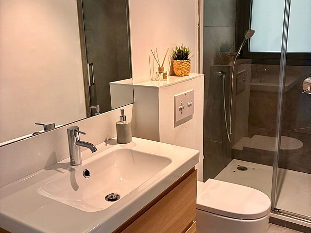 Zona de ducha moderna con alicatado gris oscuro, grifería cromada y ventana oscilobatiente.