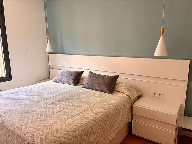 Dormitorio principal con cabecero blanco, pared decorativa en tono azul pastel y lámpara colgante.