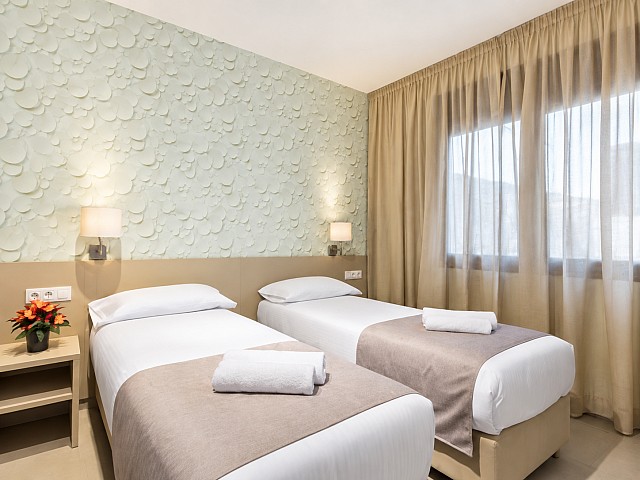 Dormitorio con dos camas individuales, ropa de cama blanca y cortinas beige